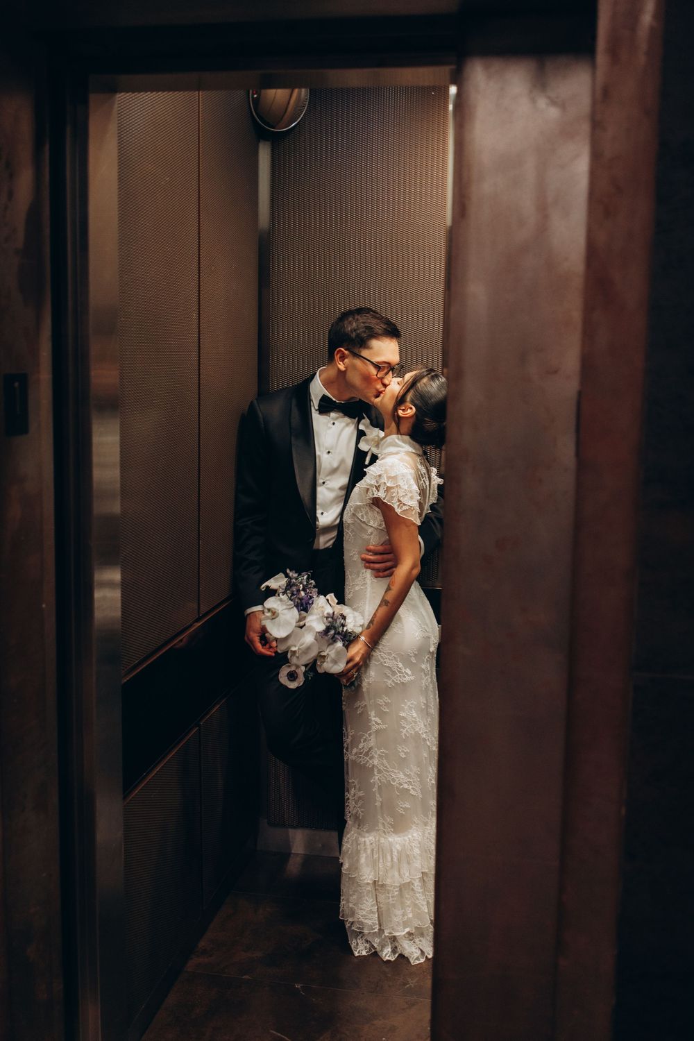 Romantic wedding couple sharing an intimate kiss in a dimly lit elevator.