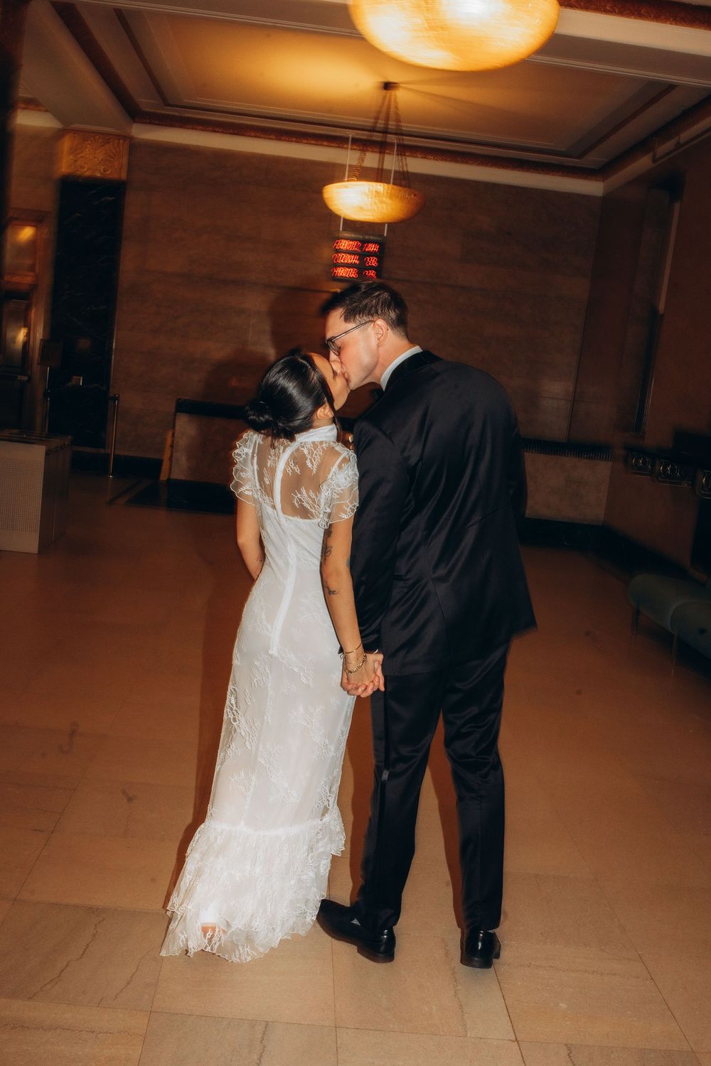A bride and groom share an intimate dance moment on an empty ballroom floor under warm lighting.