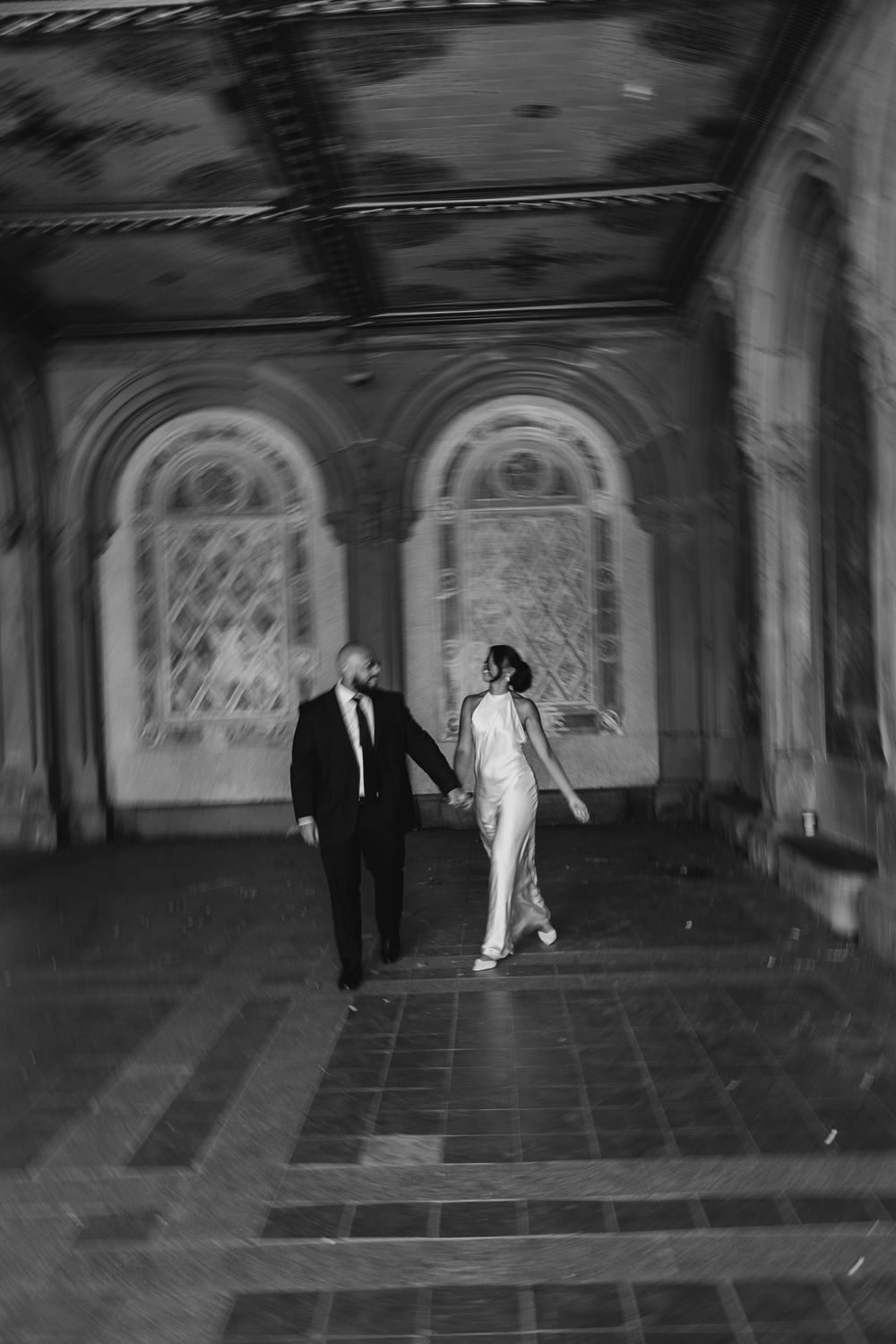 Ghostly black and white surveillance footage shows figures moving through a dimly lit historic tunnel or passageway.