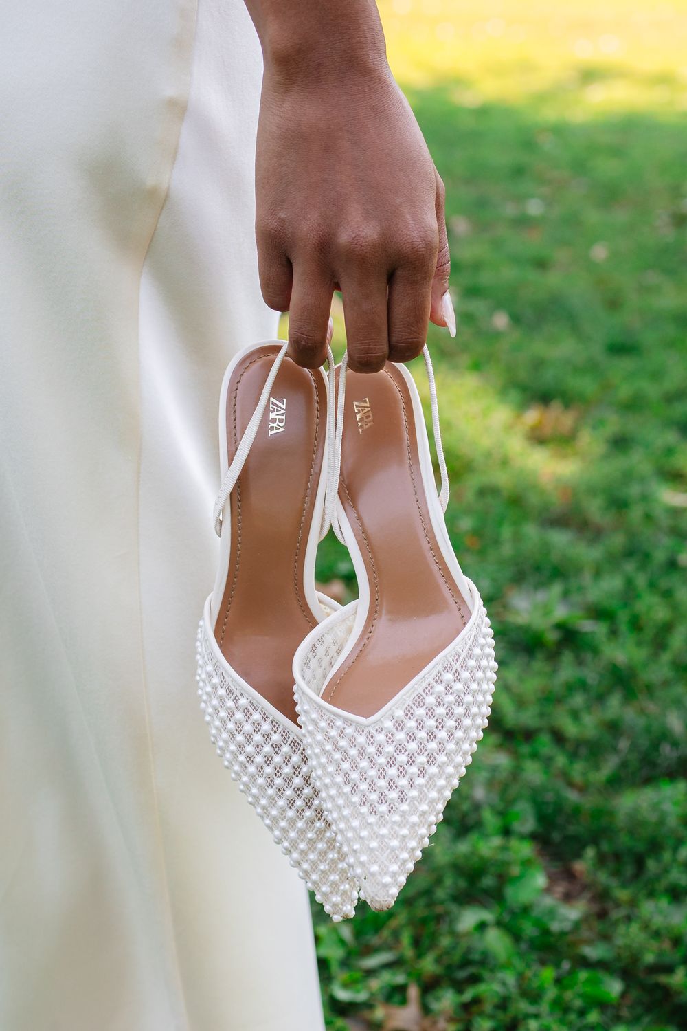 Close-up of elegant white pearl-studded bridal shoes against a grassy outdoor background.