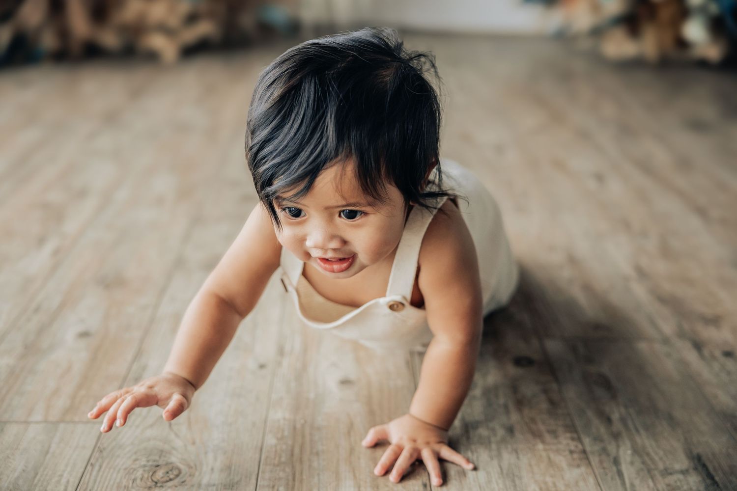 Smiling toddler crawling on hardwood floor.