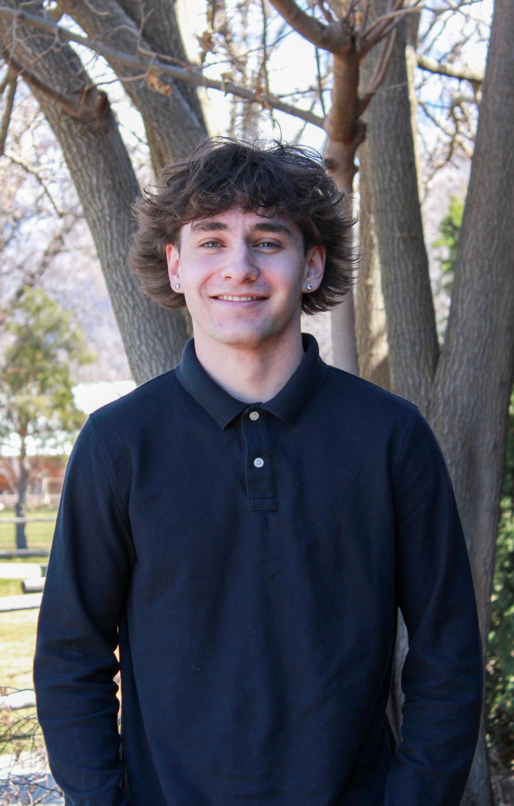 Portrait of someone in a black polo shirt standing outdoors with trees in background.