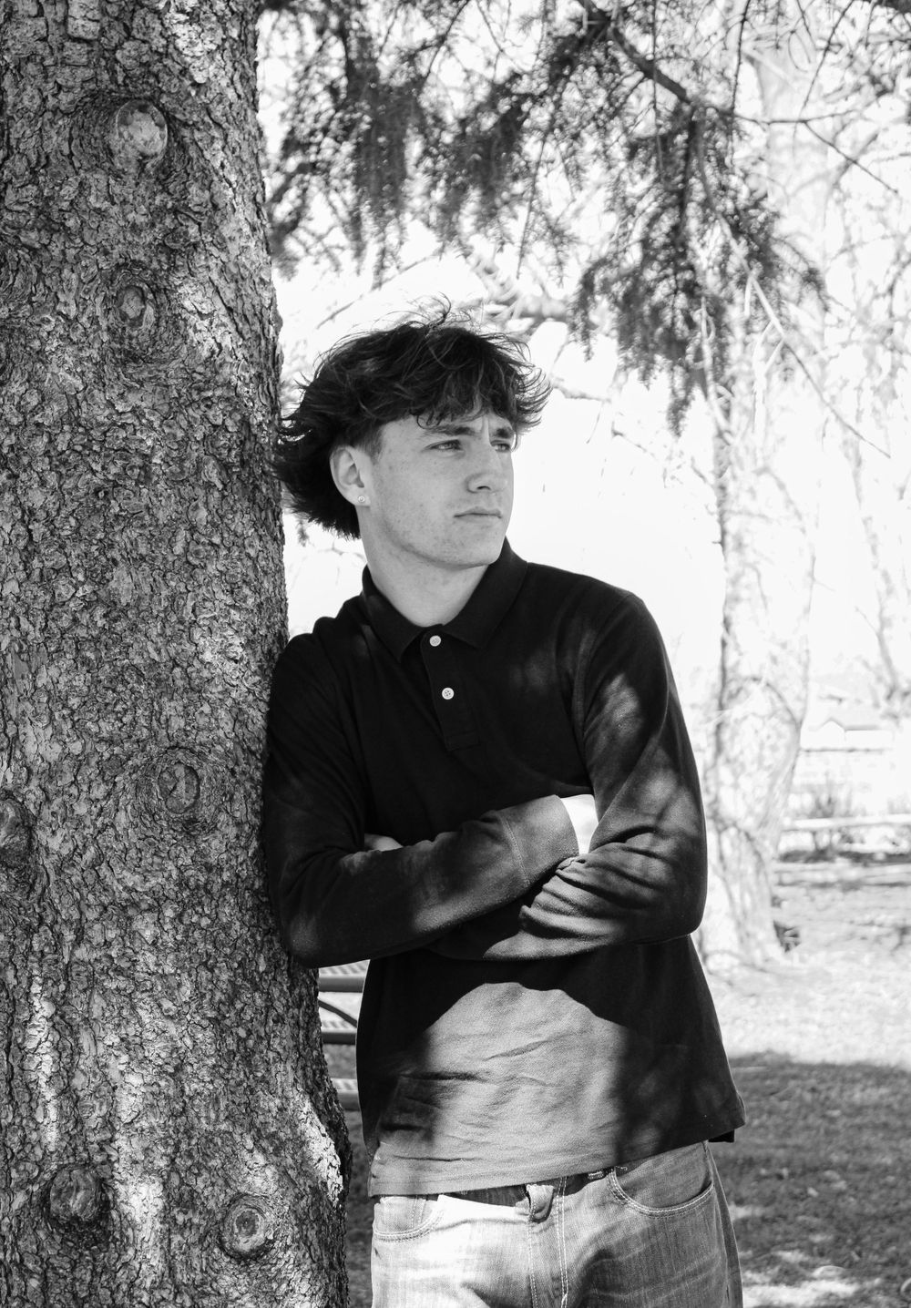 Black and white portrait of someone in polo shirt leaning against tree.