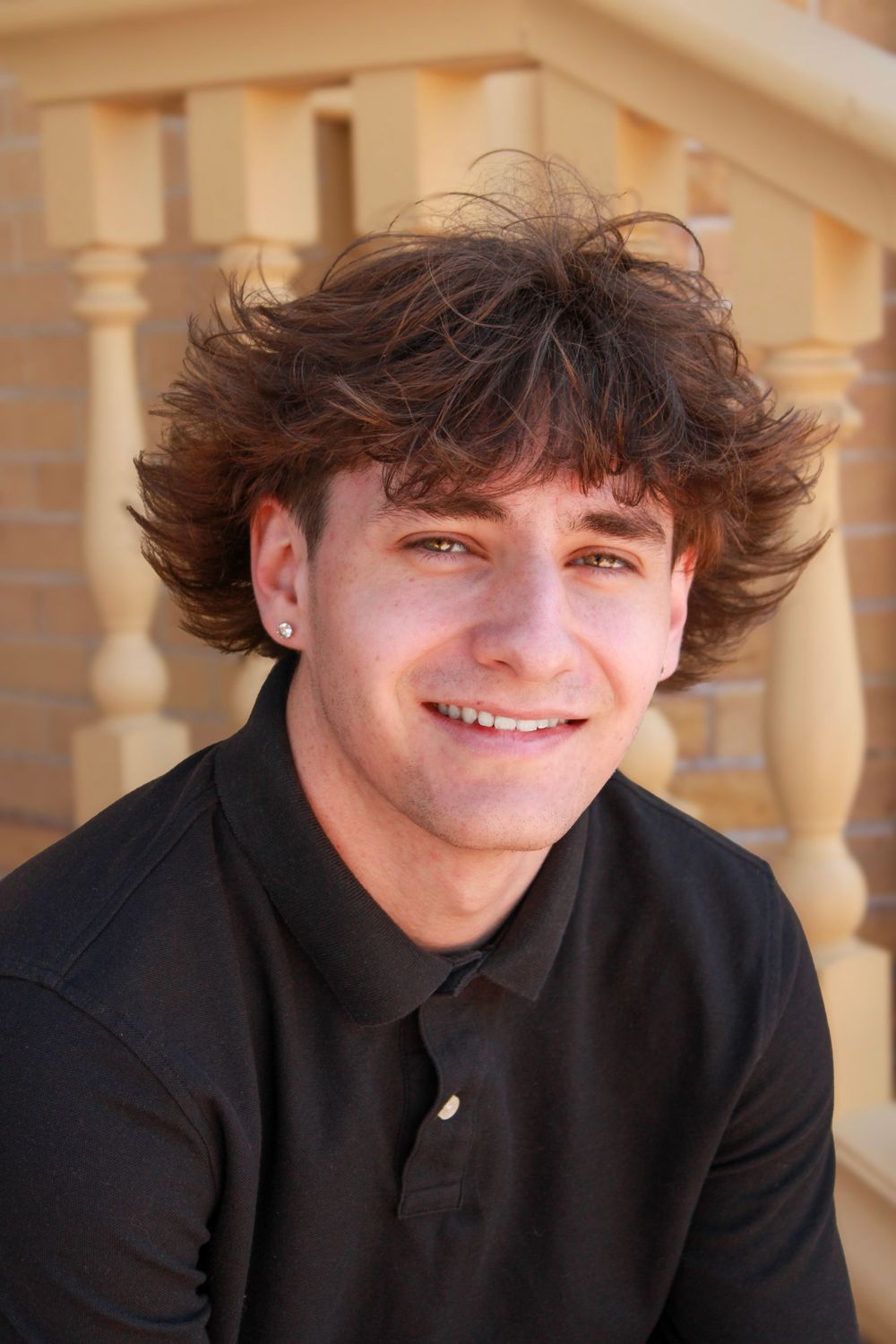 Outdoor portrait with decorative pillars showing person in black polo smiling.