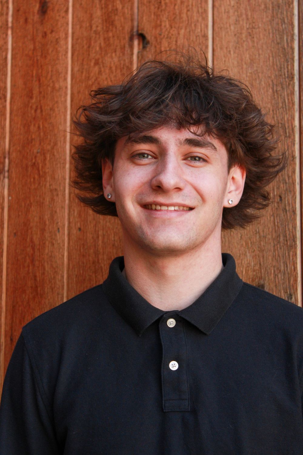 Portrait against wooden background showing person in black polo with an earring.