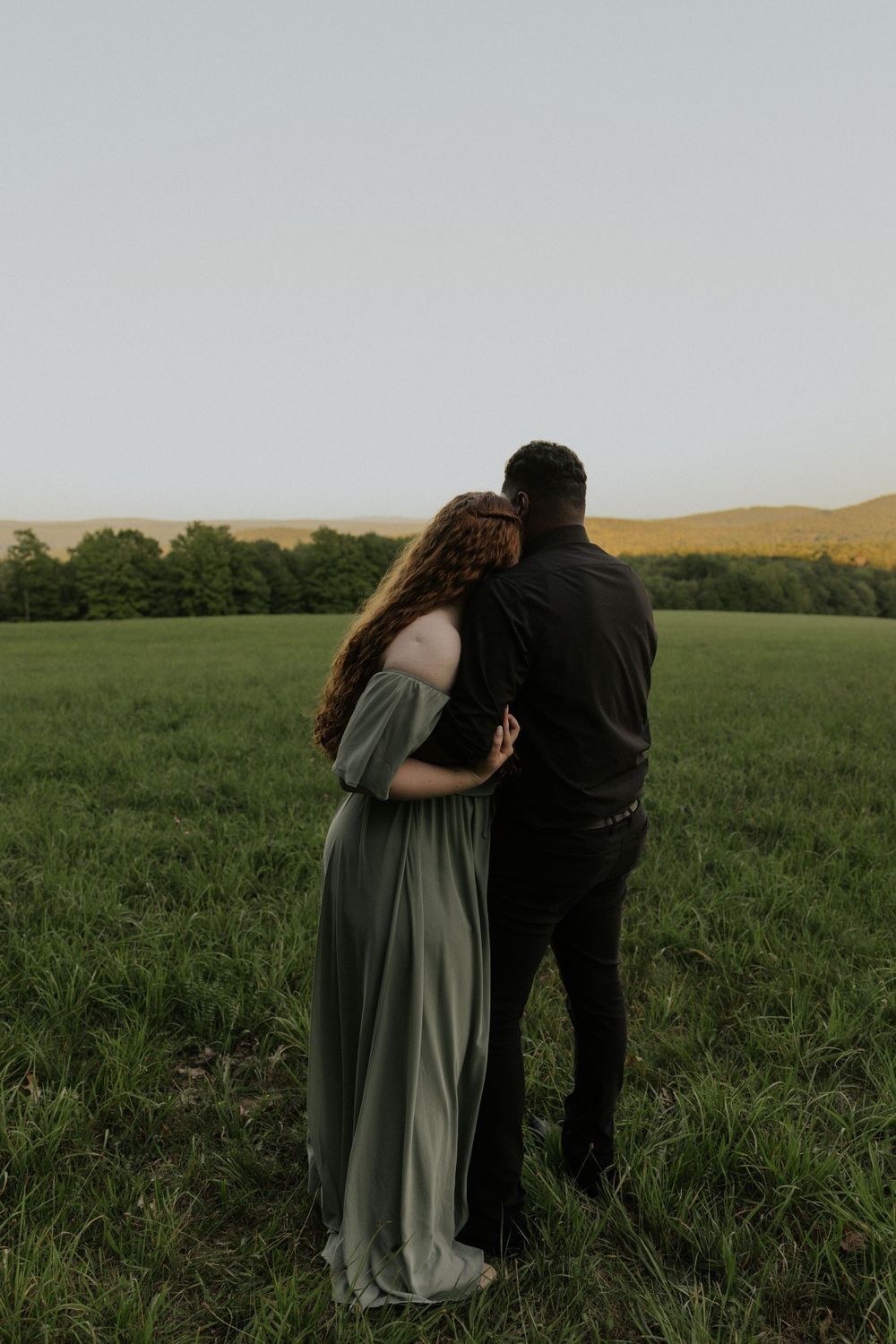 A romantic couple poses together in a serene field with mountains on the horizon.