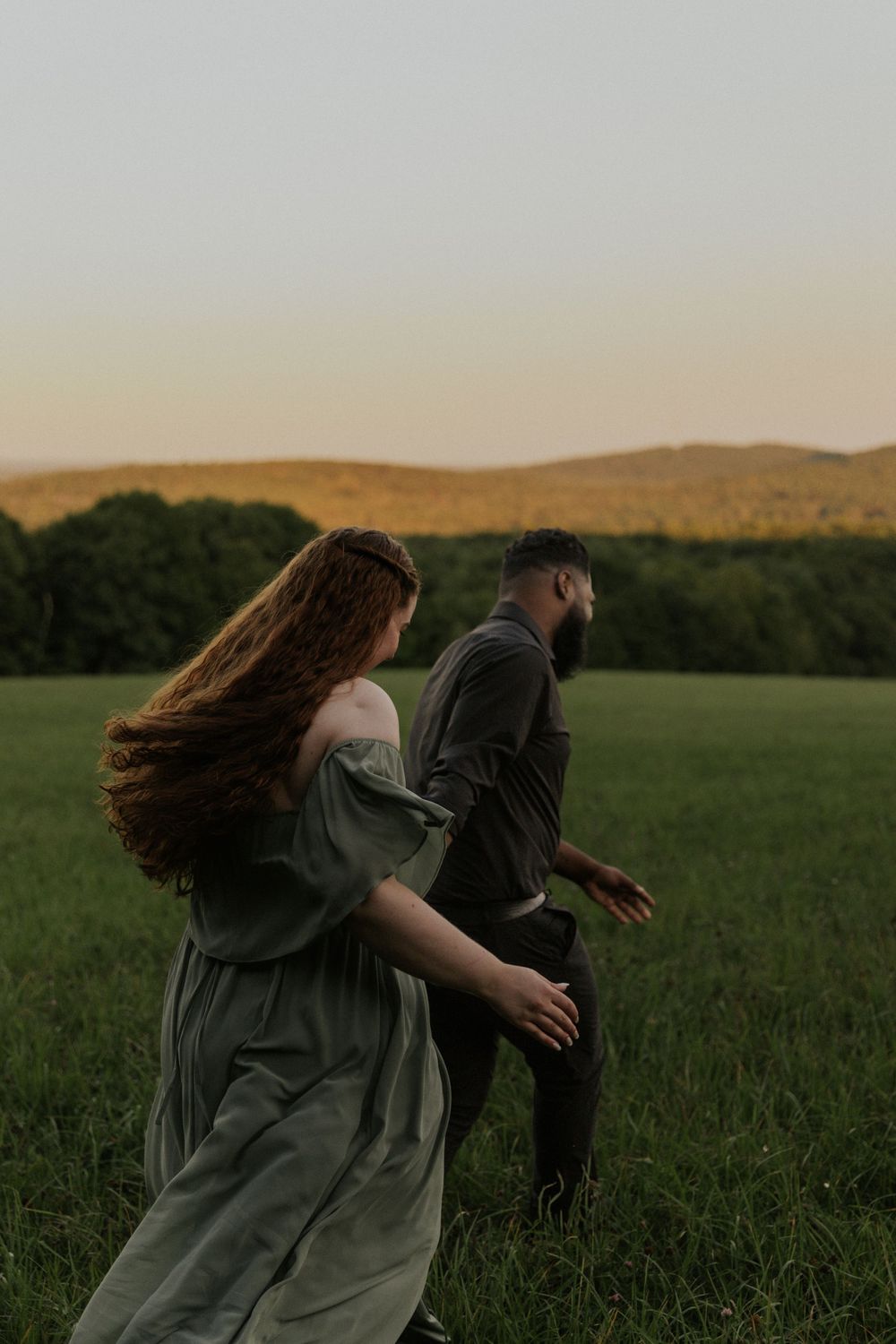 Two people dance playfully through a green meadow at dusk.