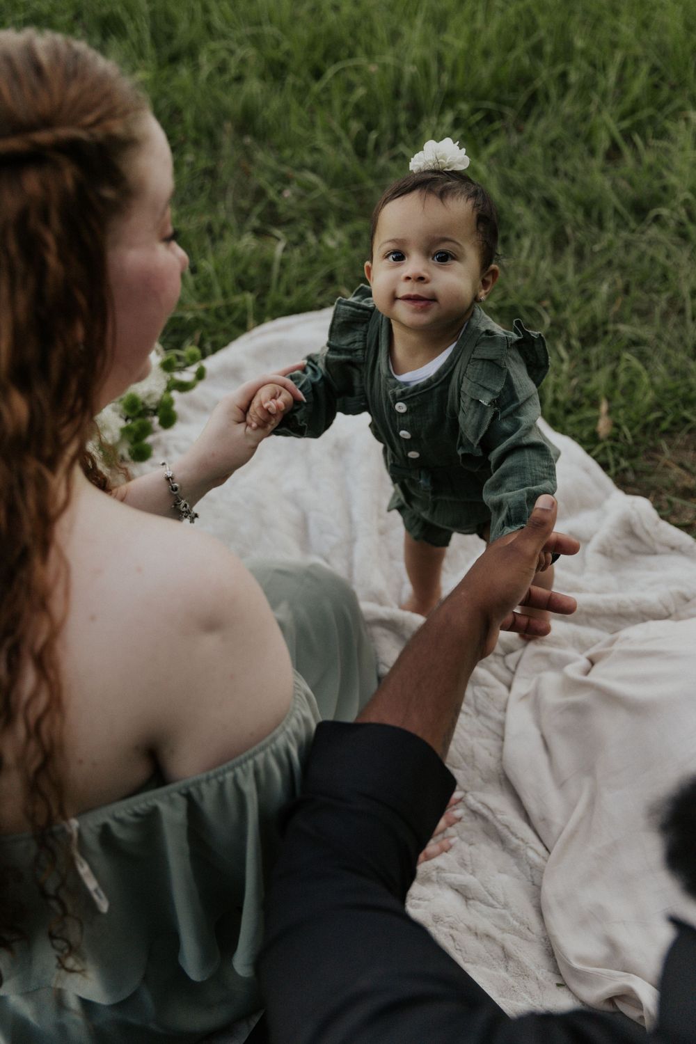 A tender moment between adults and child on a picnic blanket in a grassy field.