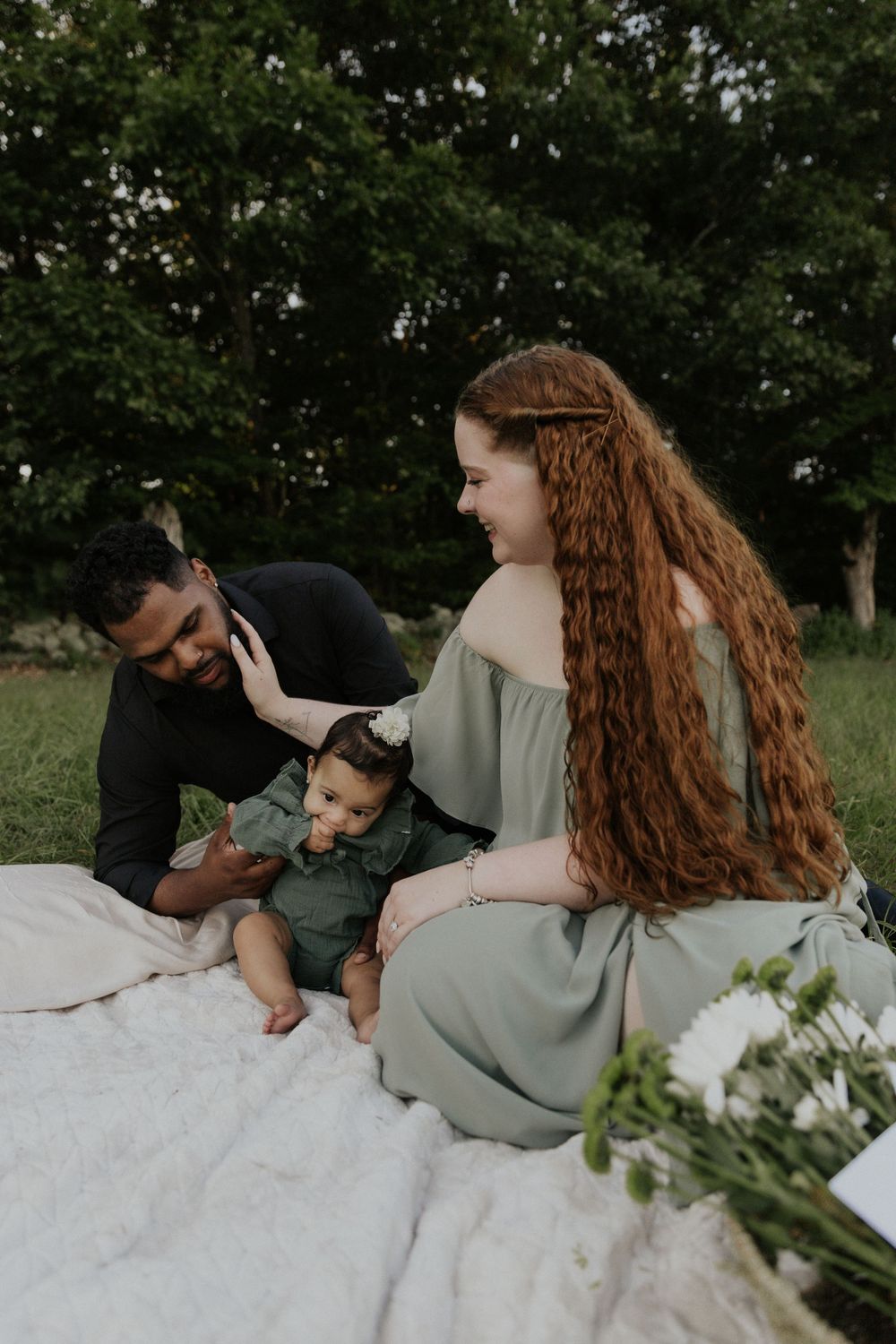 People share intimate moments while lounging on a white blanket in a sunny meadow.