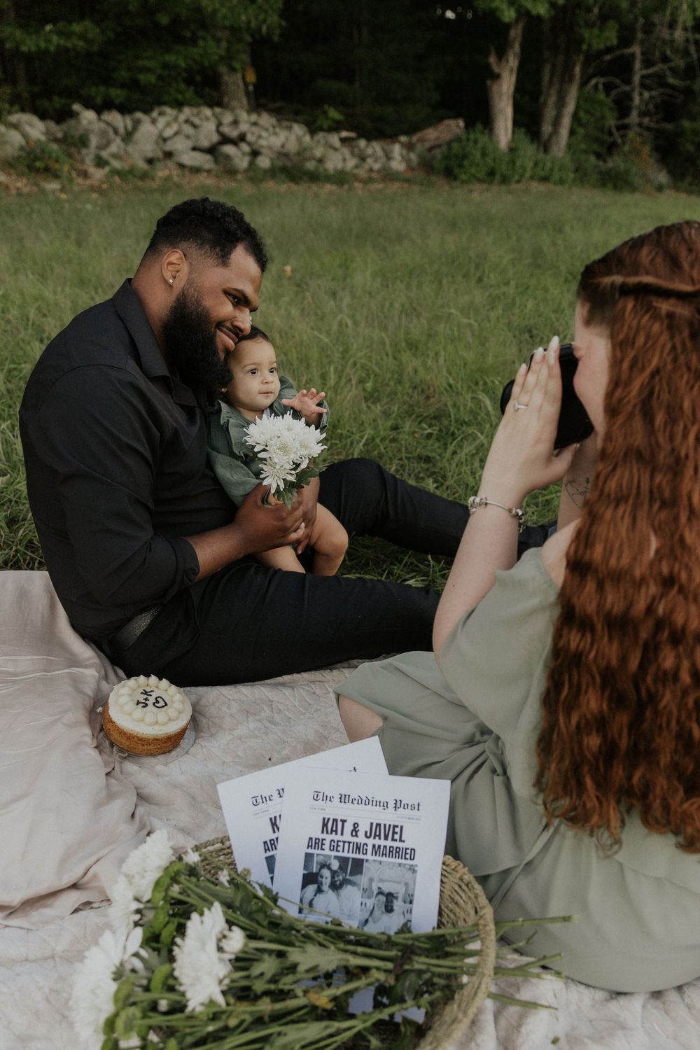 Family picnic scene with vintage newspaper and flowers on blanket in grassy field.