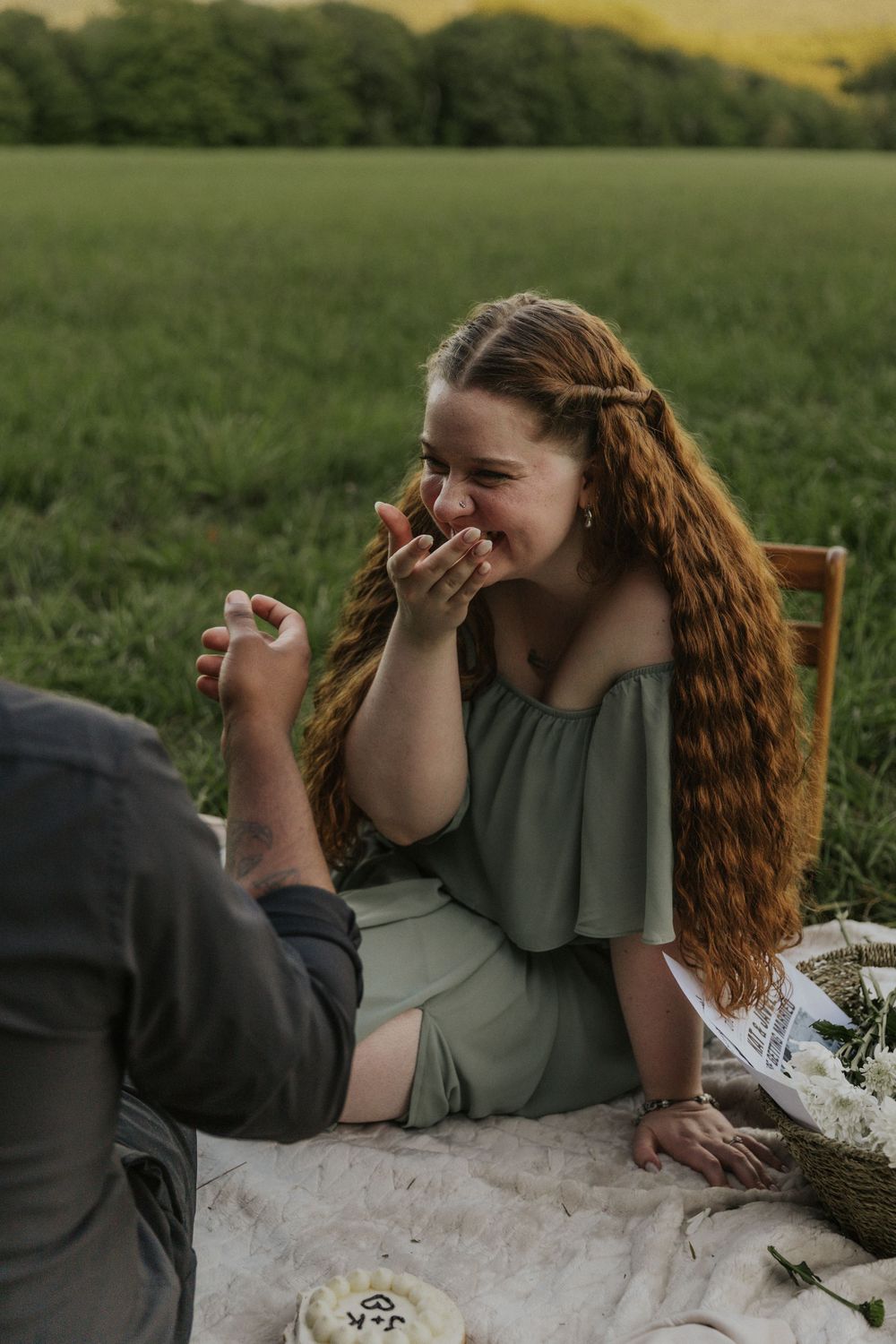 A couple laughs together during an intimate picnic moment in a green field.