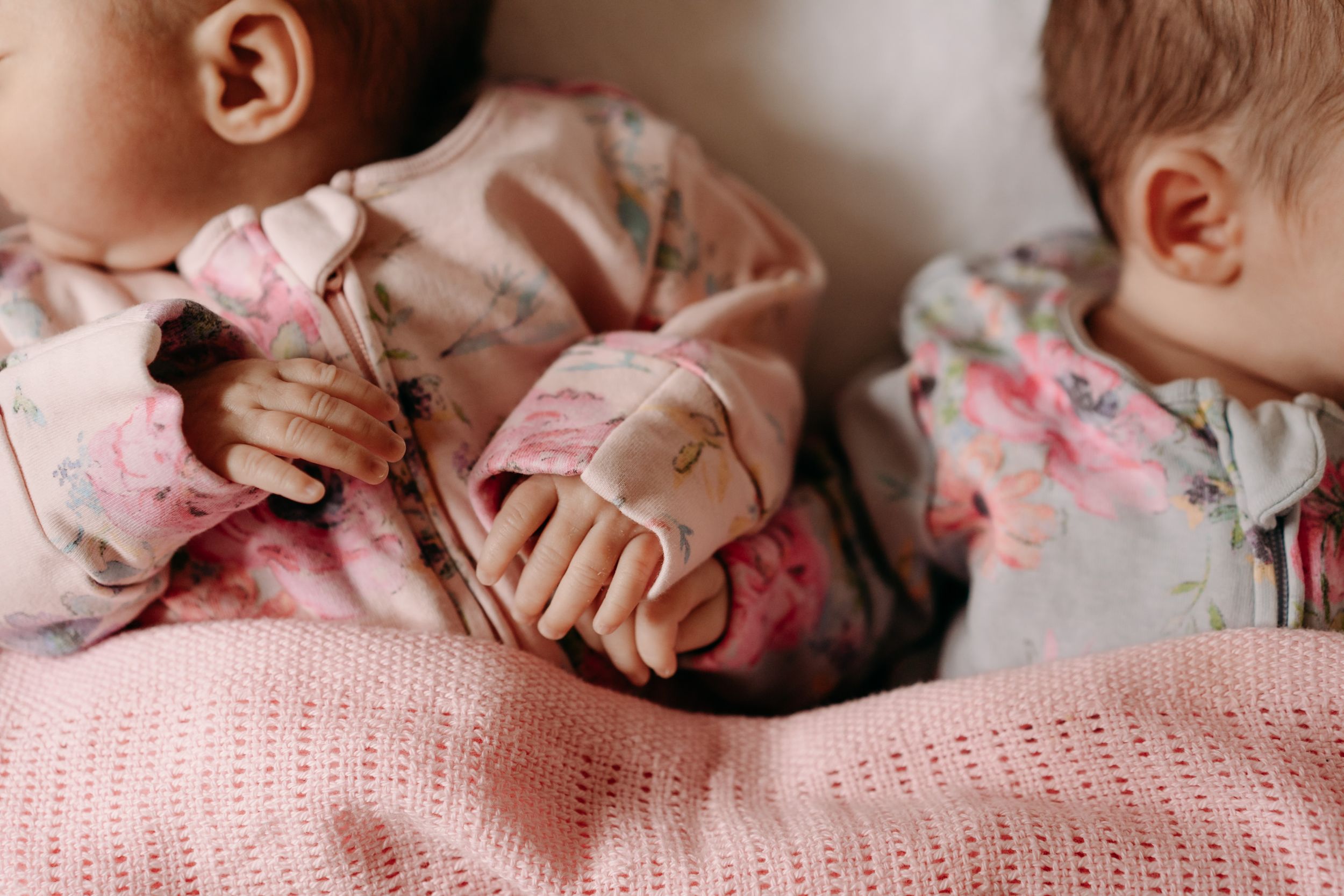 Close-up of small hands holding while resting on a soft pink knitted blanket.