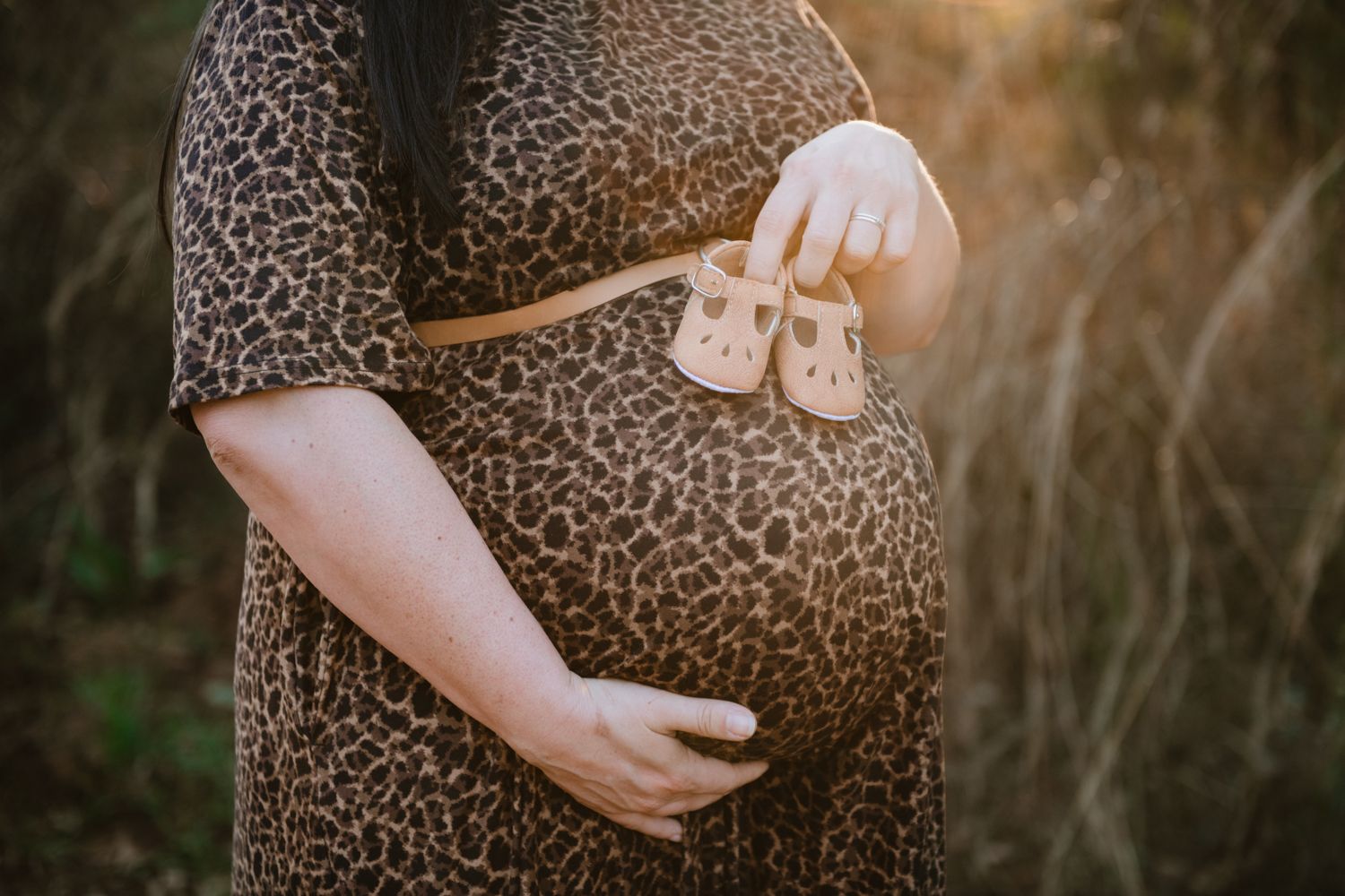 Pregnant woman posing outdoors, holding her baby bump.