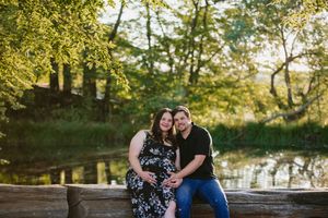 Long shot image of a couple sitting next to each other with the dam behind them for their maternity shoot.