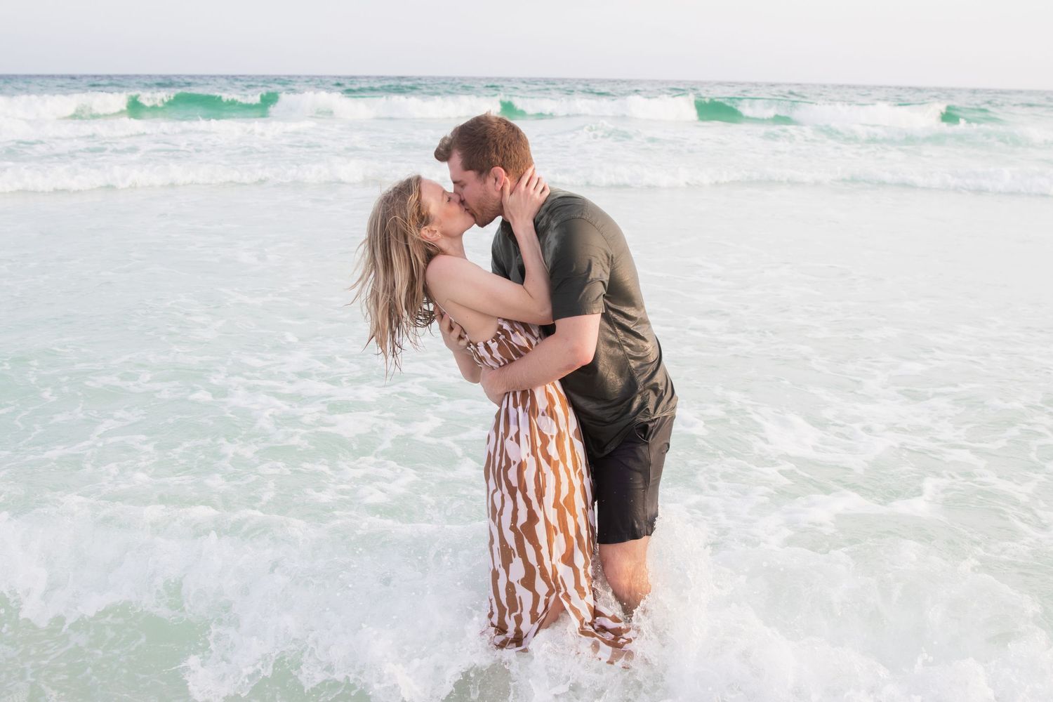 Romantic couple embracing in the ocean waves during sunset photoshoot.