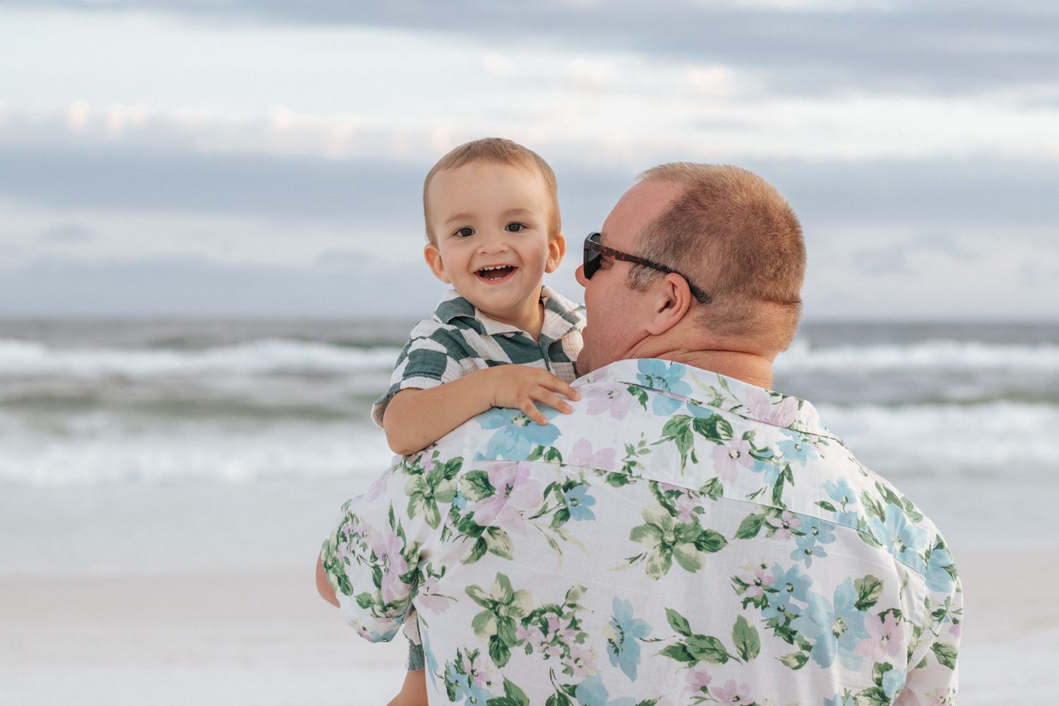 Sweet bonding moments shared on the beach with white floral shirts against ocean waves.