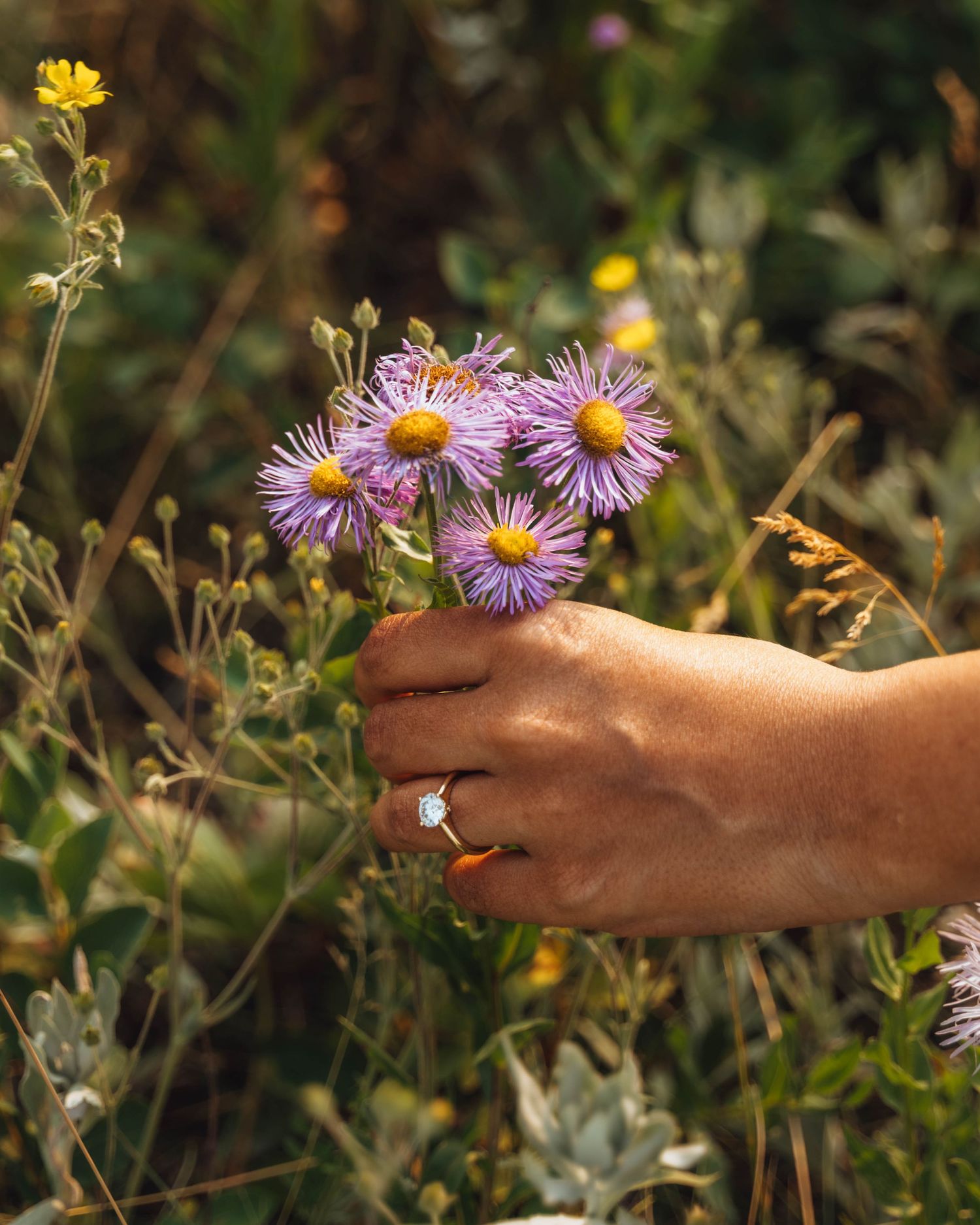 A hand holds flowers and a wedding ring. Banff engagement photography.