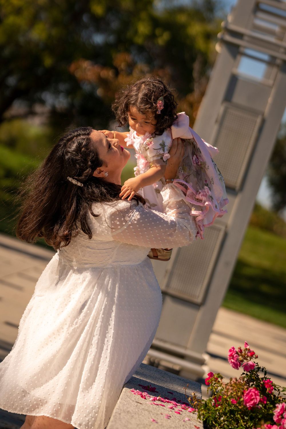 Tender outdoor moment captured in sunlight with white dress and pink flowers.