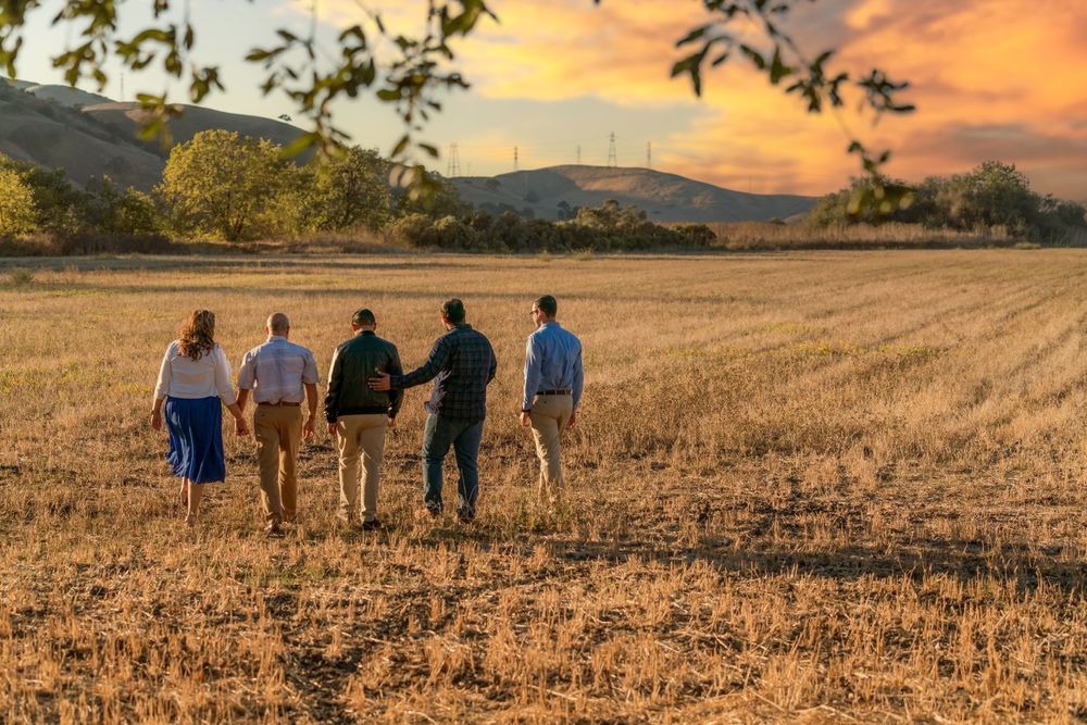 Five people walk away from camera across a harvested field at sunset.