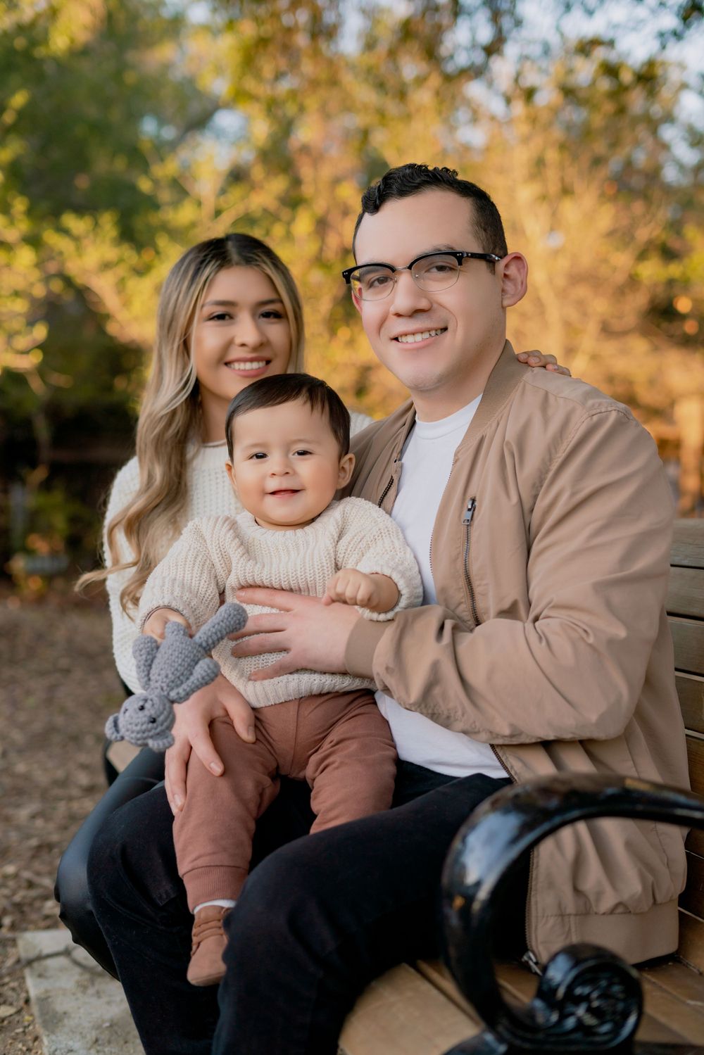 A family sits together on a wooden bench during an autumn outdoor photo session.