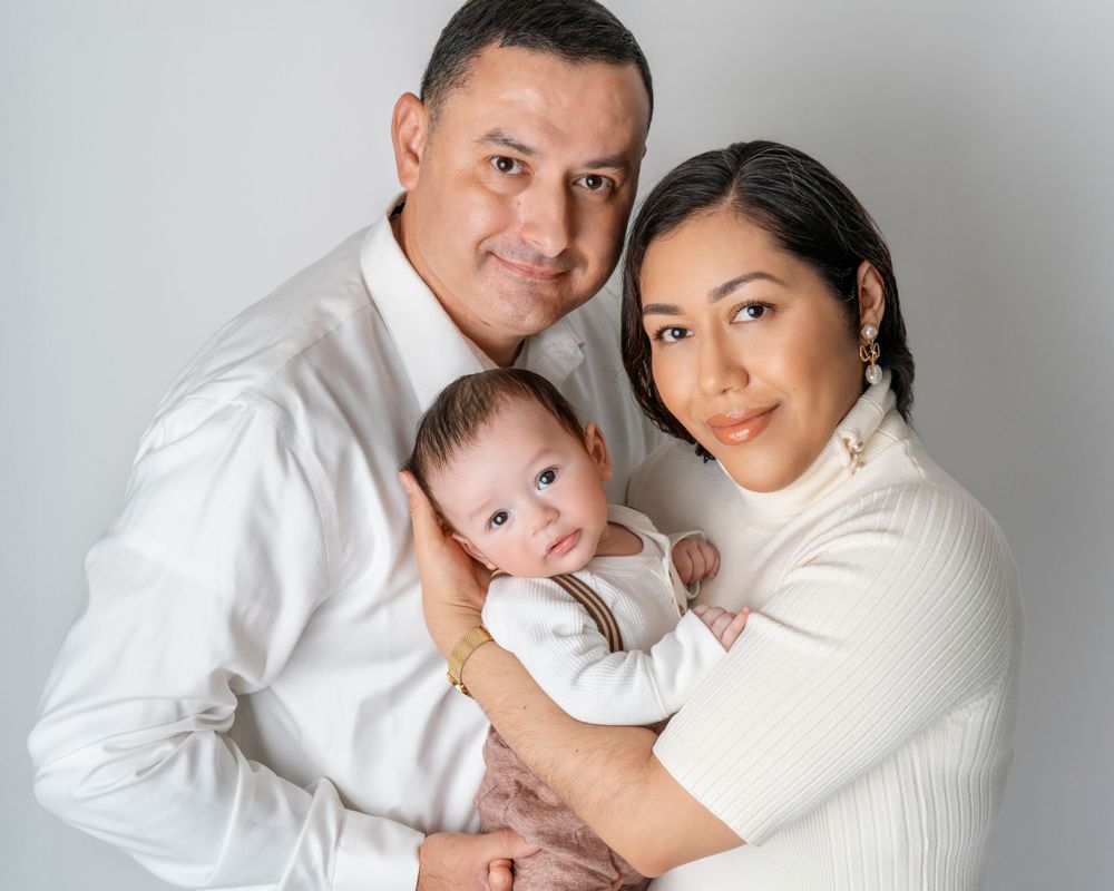 A family poses together in white clothing for a studio portrait with their baby.