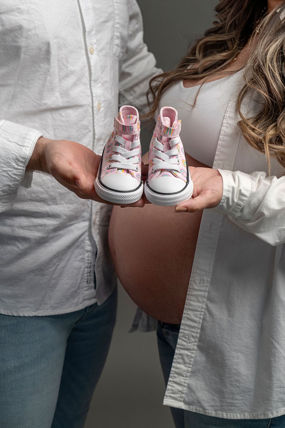 Hands holding tiny pink baby shoes with white background.