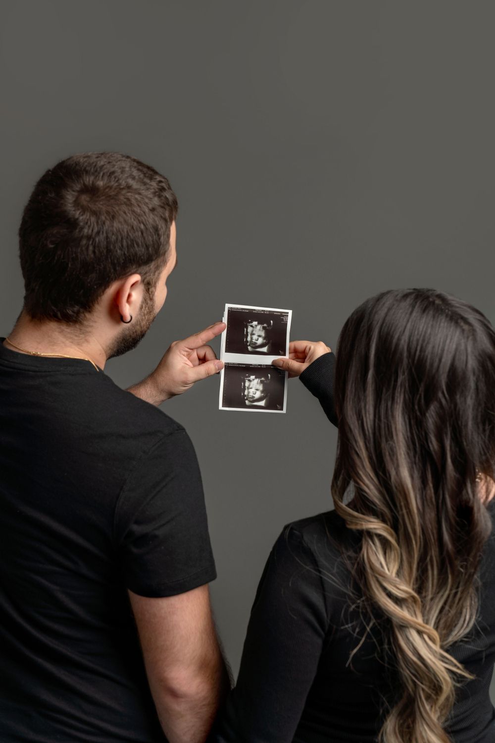 Couple looking at ultrasound photos against dark background.