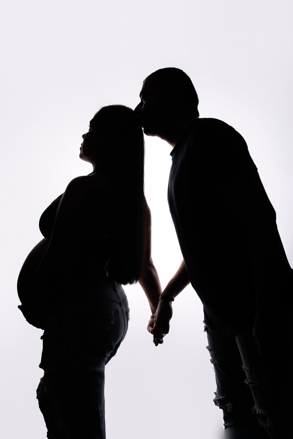 Silhouette of expecting couple in intimate pose against white background.