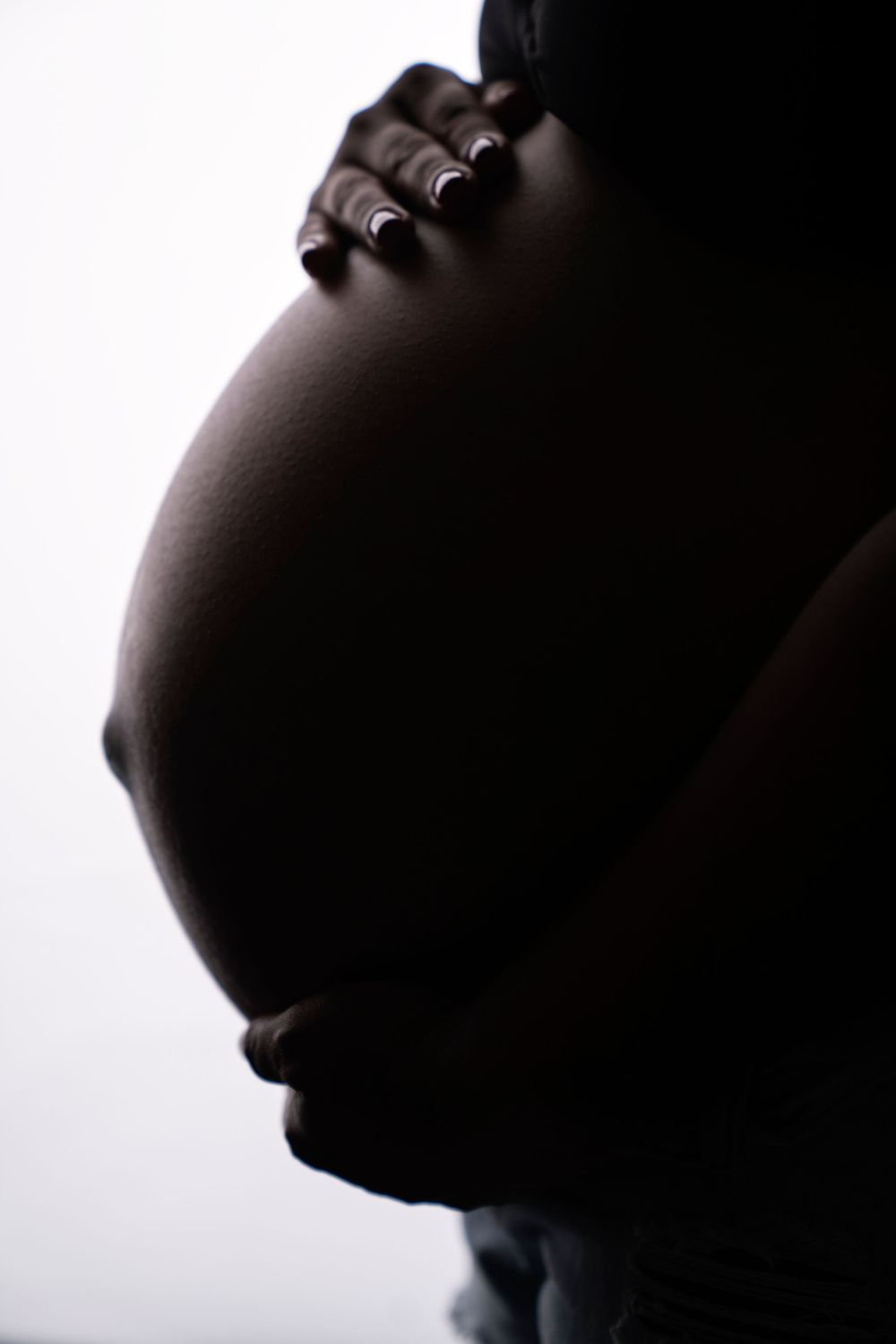 Artistic silhouette of pregnant belly with hands resting on top.