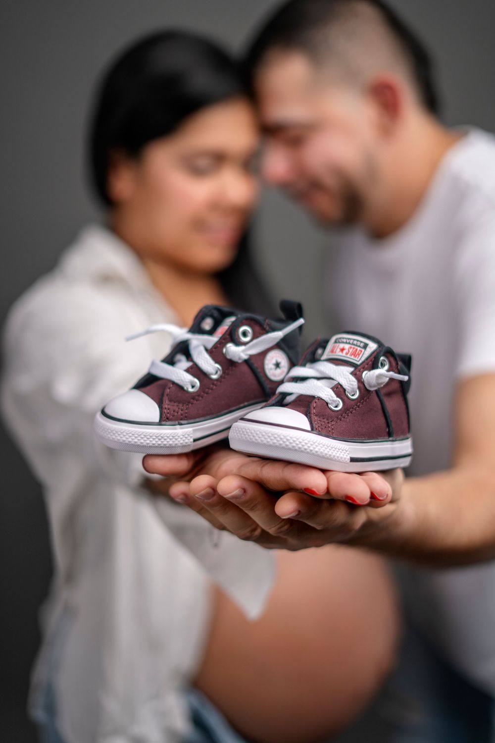 Small brown baby sneakers held up in focus with blurred couple in background.
