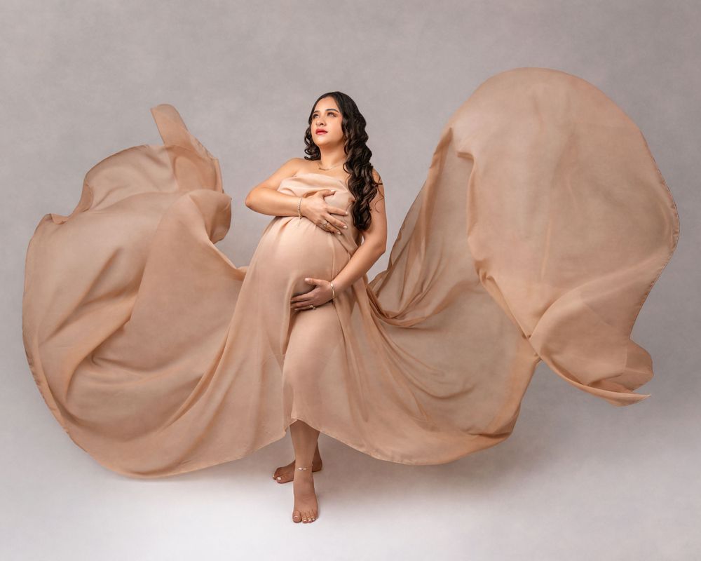 Flowing beige fabric creates dramatic movement around an expectant mother in a studio maternity photo.