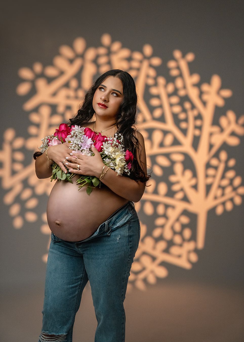 Maternity portrait with floral bouquet against illuminated tree wall art.
