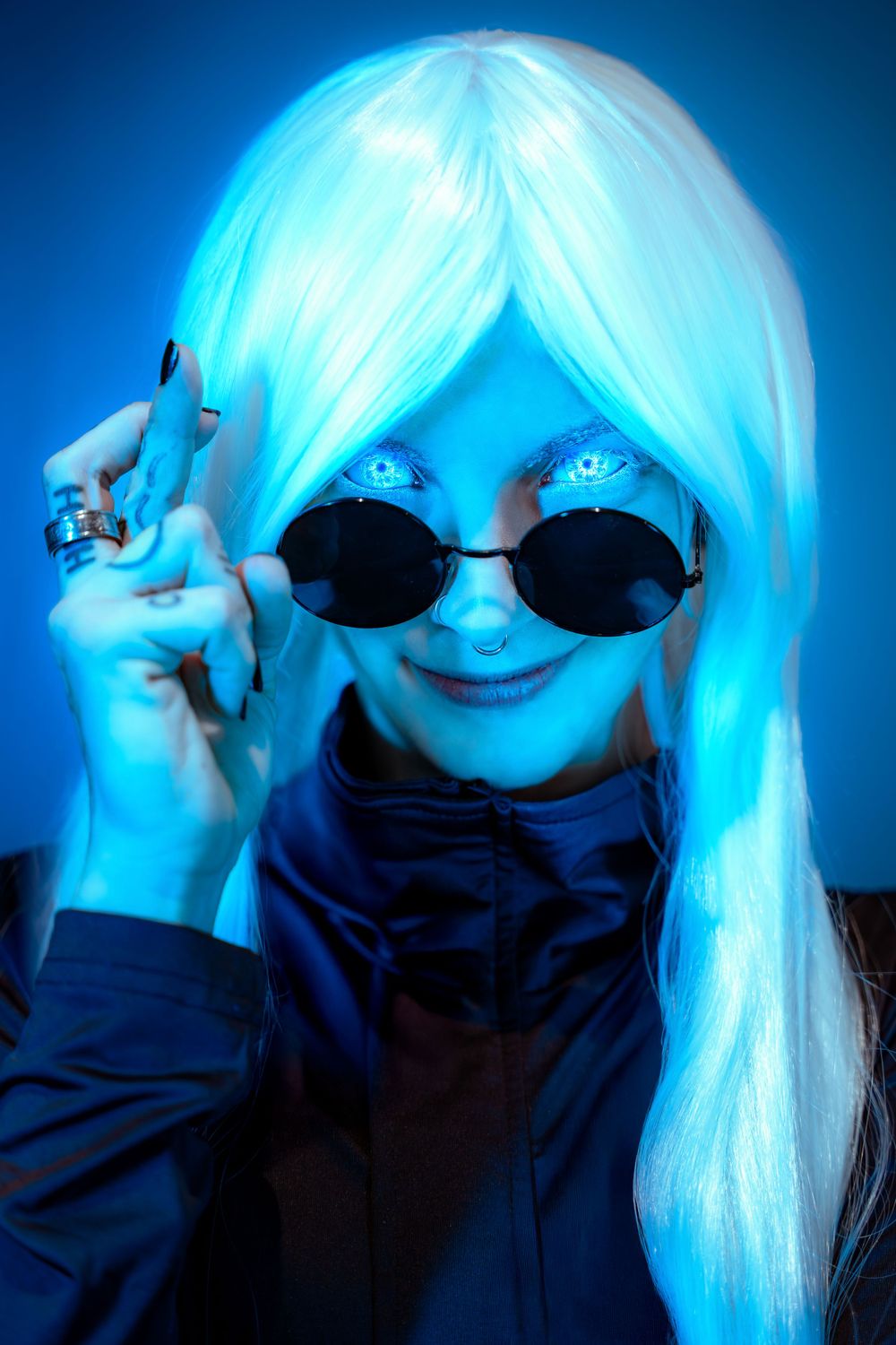 Portrait of gender-bent Satoru Gojo cosplay wearing sunglasses under blue lighting.