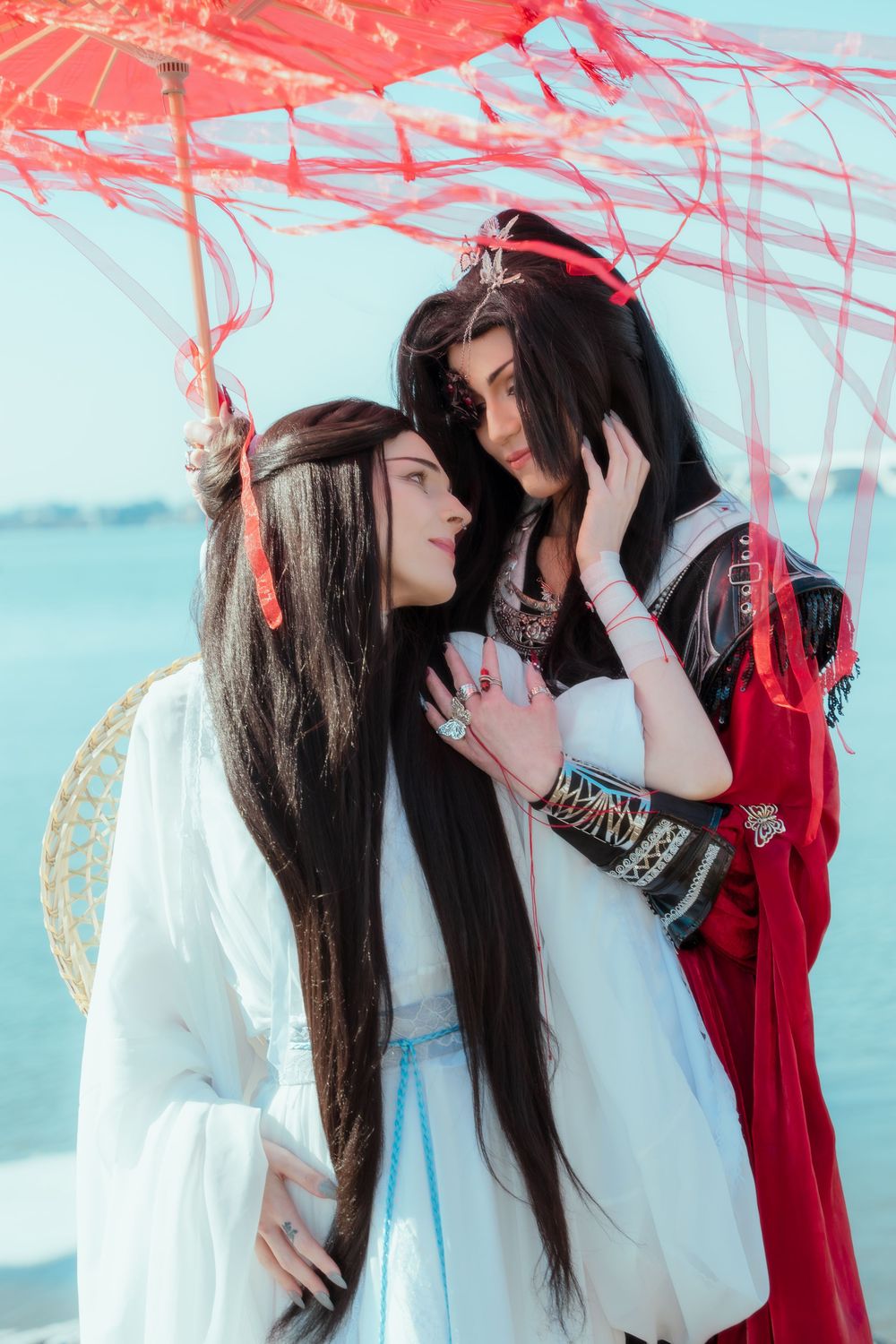 Xie Lian and Hua Cheng cosplay from Heaven's Official Blessing beneath a red umbrella.