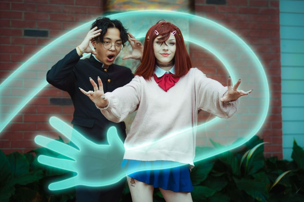 Cosplay portrait of Momo and Okarun from Dan da Dan with glowing ghost hands.