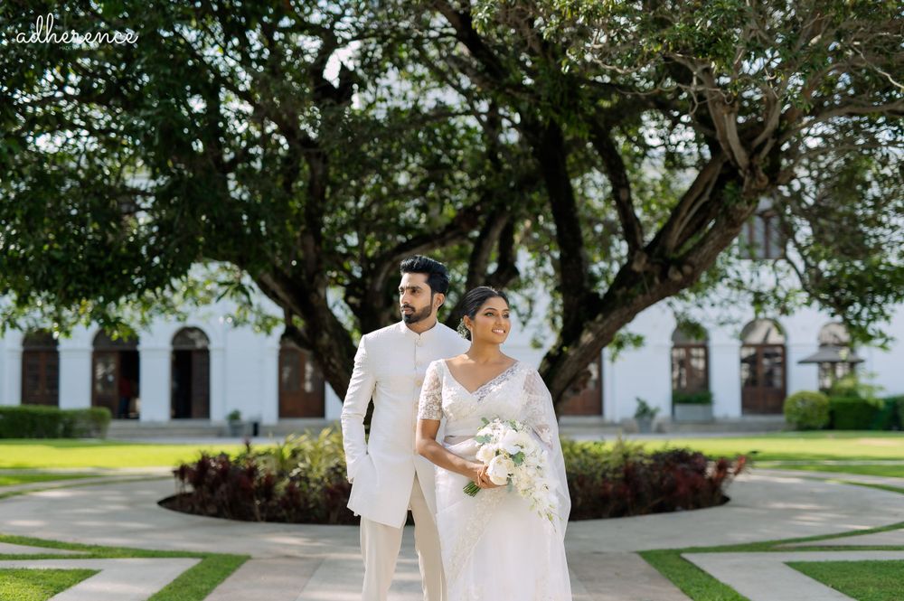 Wedding couple in all-white attire pose outdoors with classic architecture in background.