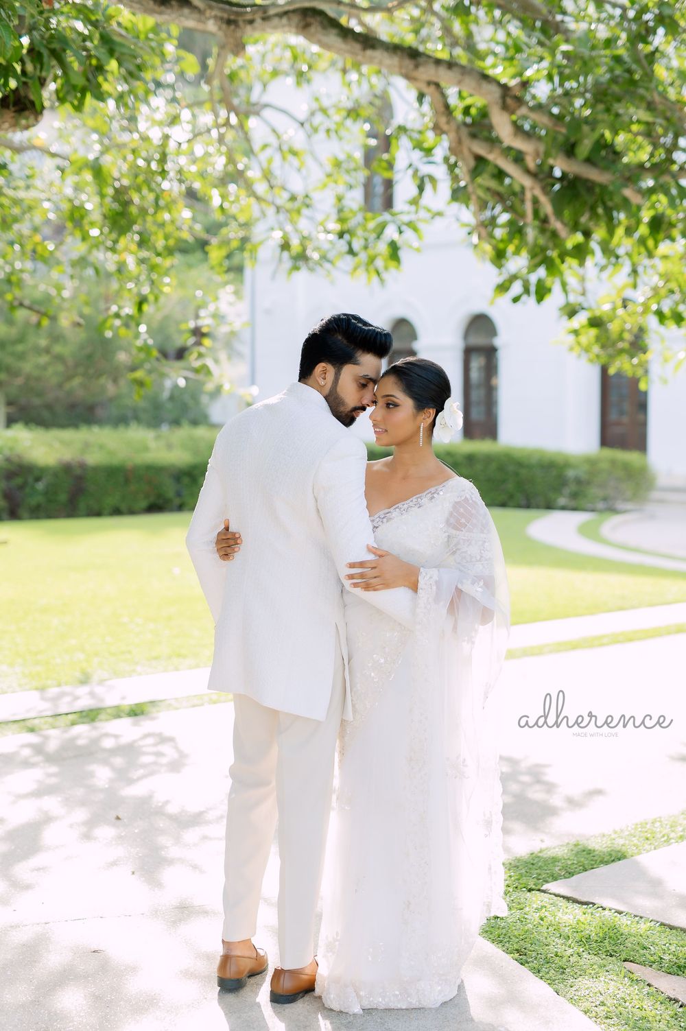 Romantic wedding portrait of couple in white attire embracing in garden setting.