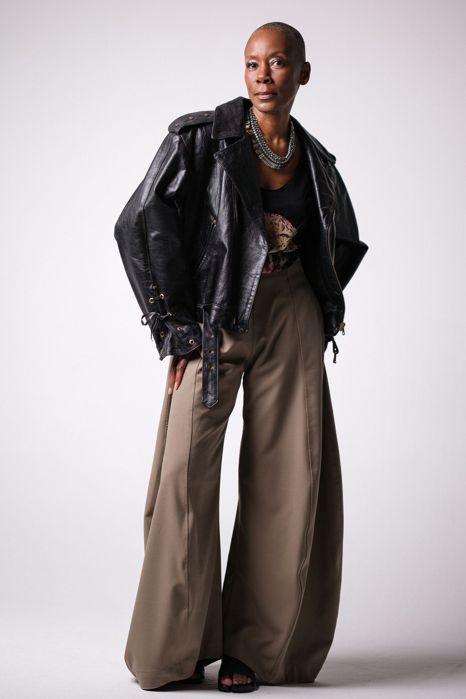 Fashion portrait in white studio wearing oversized black leather jacket and wide-leg pants.