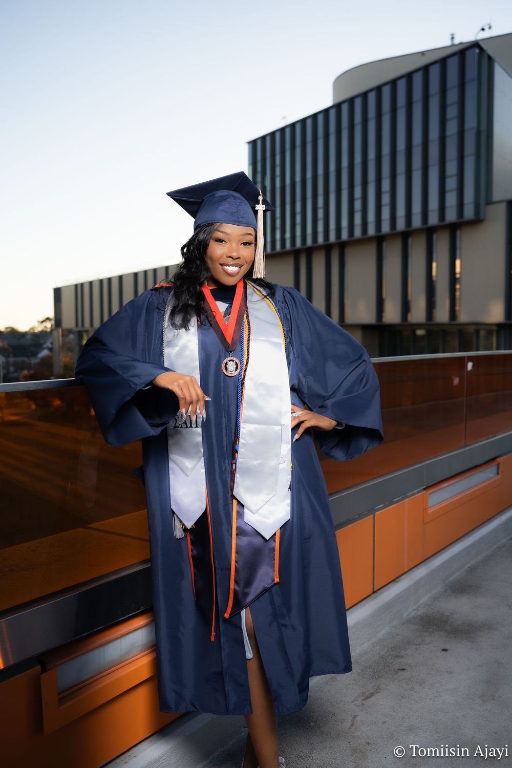 Graduate in navy blue cap and gown poses confidently on outdoor steps during graduation photo session.