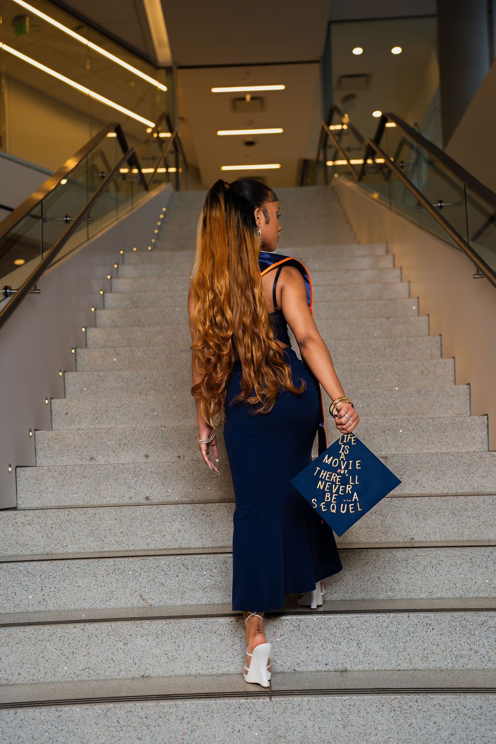 Person in a navy blue dress and white sneakers walks up concrete stairs with a blue handbag.