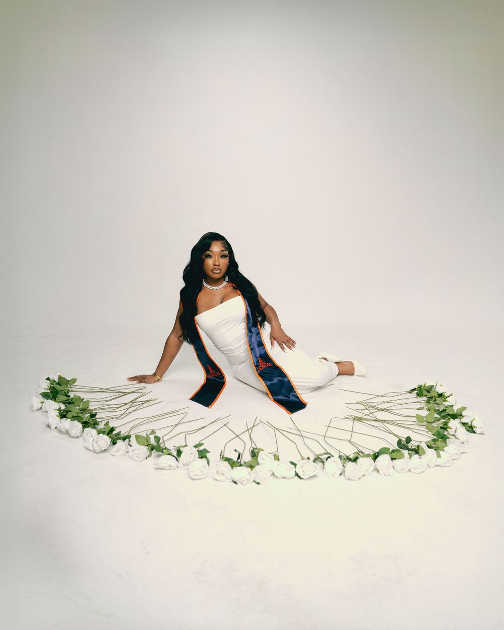 A figure in a flowing white dress lies gracefully among delicate green vines and leaves on a light background.