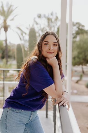 Casual portrait leaning against a white pillar with palm trees in the background.