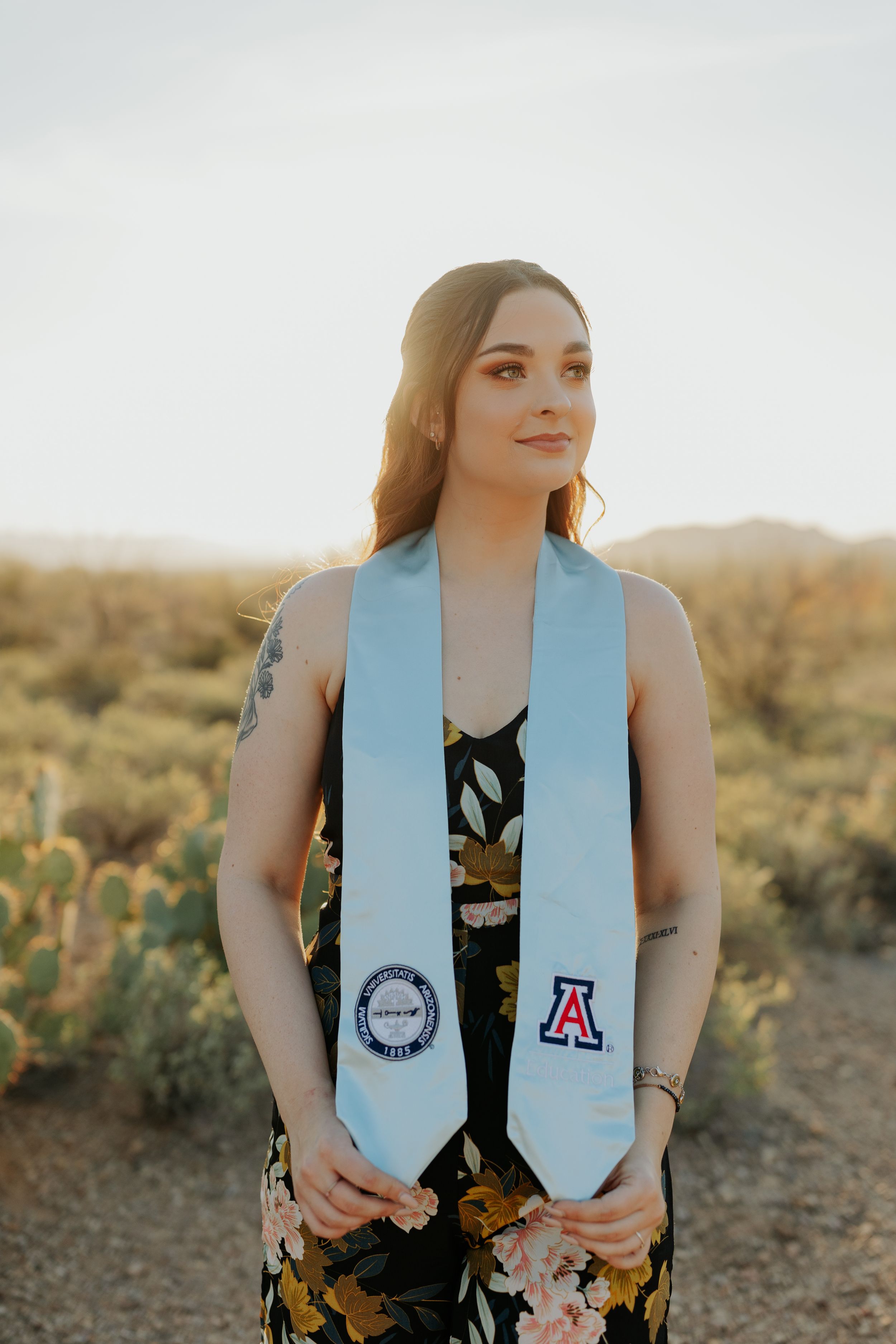Graduate wearing light blue graduation stole in desert setting with cacti.
