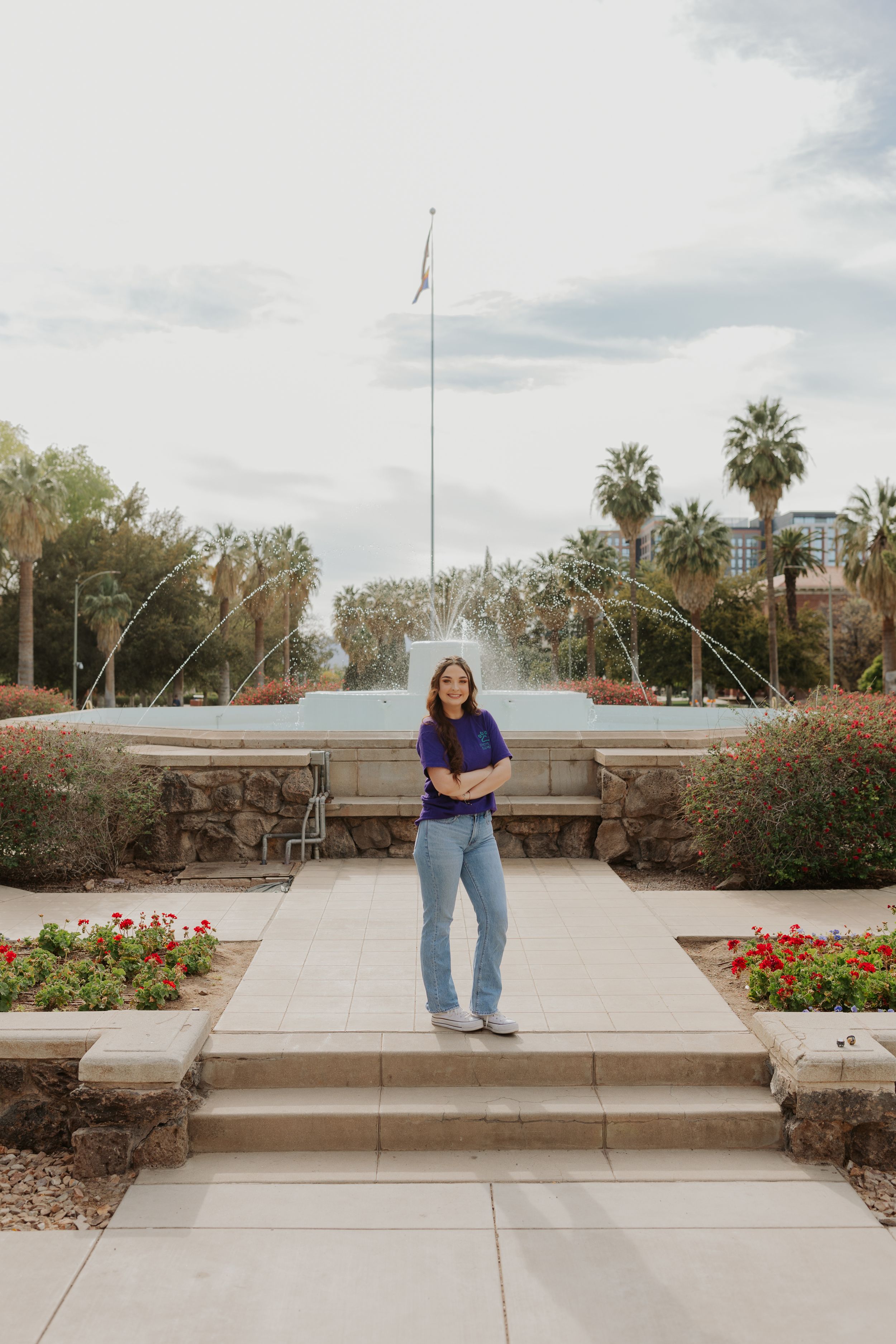 Person in casual wear poses on concrete steps with desert garden and flagpole visible.