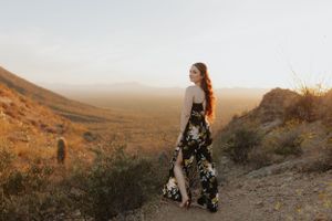 A desert photoshoot featuring someone in a floral dress against rugged mountain terrain.