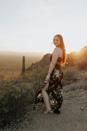 A figure in a floral dress poses gracefully on desert terrain during golden hour.