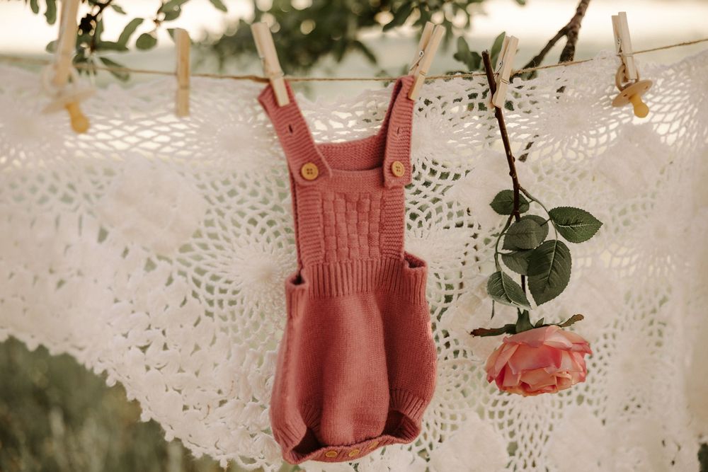 Pink knit romper and floral dress hanging on delicate lace background with eucalyptus sprigs.