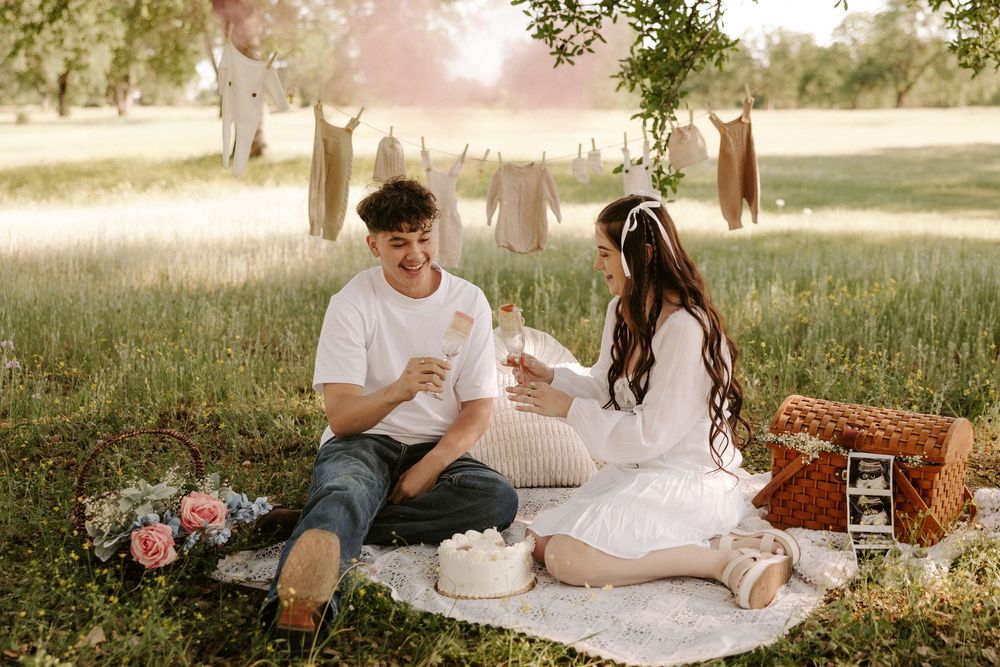 A couple enjoys a romantic outdoor picnic with wine and snacks in a sunlit meadow.