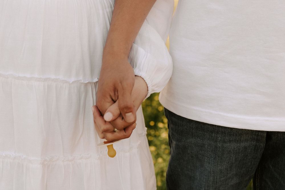 Close-up view of hands holding white paper hearts in a row against a bright background.