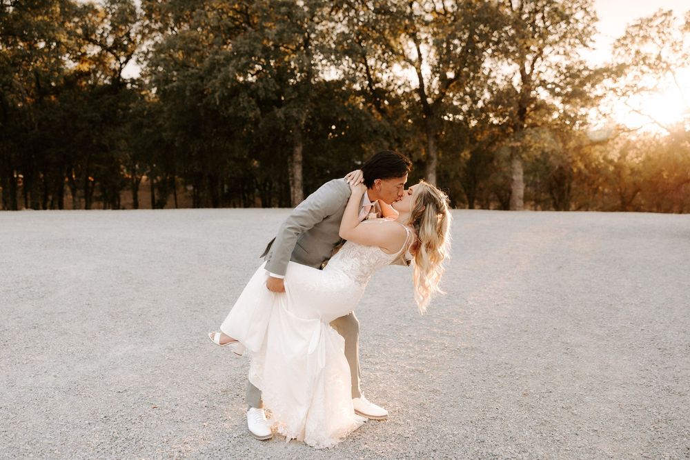Couple in white attire dances together in a snowy field during golden sunset hour.